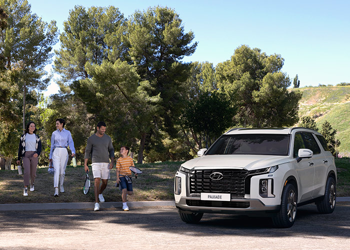 Familia caminando en grupo junto a una Hyundai Palisade color blanca