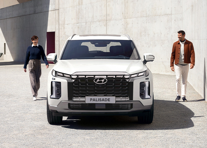 Hombre y mujer caminando por los costados de una Hyundai Palisade color blanca